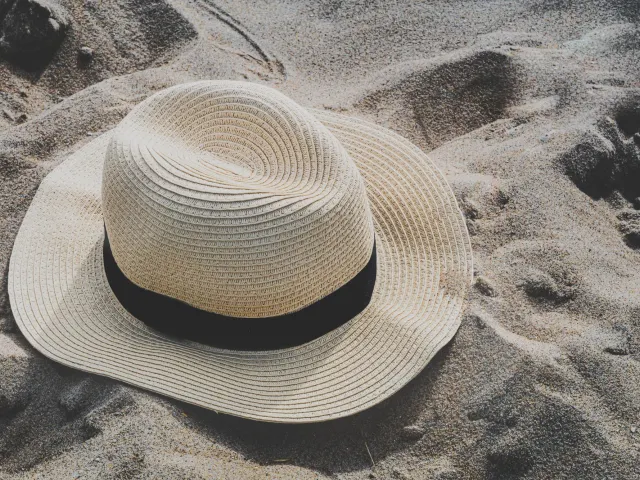 Natural woven sun hat with a black ribbon band resting on sand